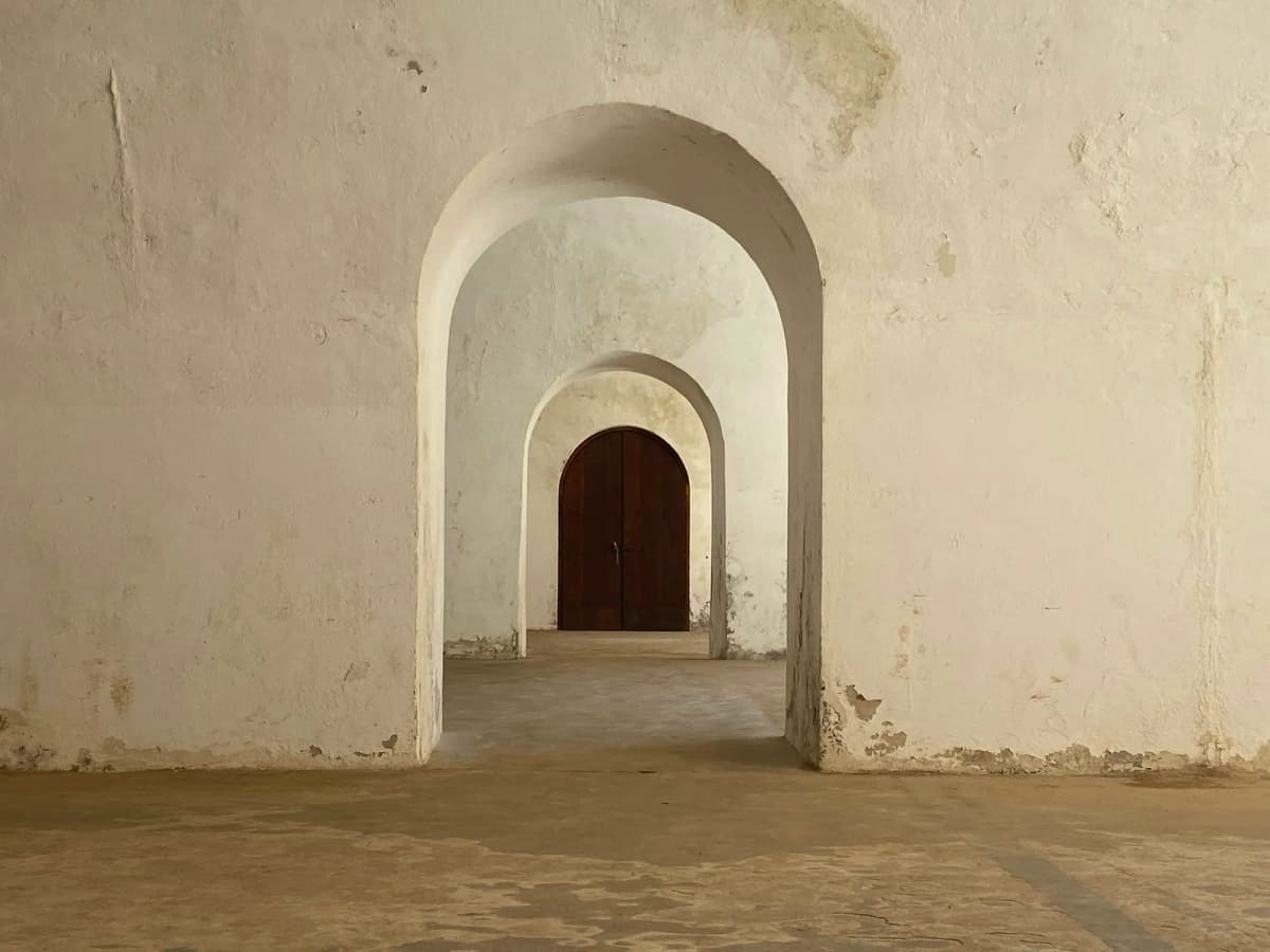 A row of plaster arches receding toward a wooden door