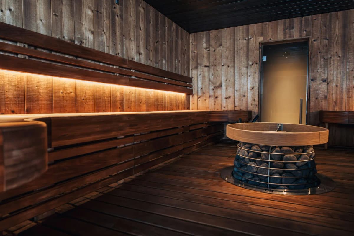 A timber sauna lounge with a round stove and a band of warm light